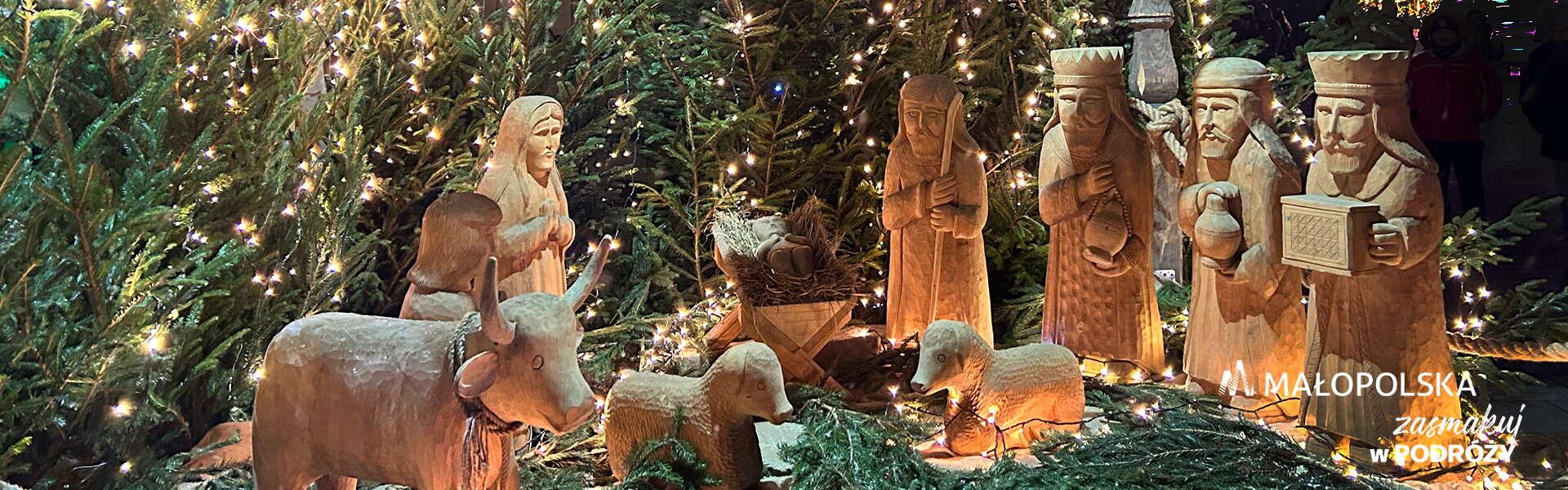 Drewniane figurki Dzieciątka Jezus, Maryi, Józefa, Trzech Króli, woła i owiec ustawione w szopce, otoczone iglastymi drzewkami