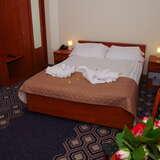 Pokój w hotelu, zasłane podwójne łóżko, szafki, szafa, lampki.
