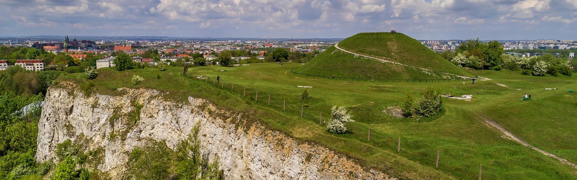 A large, green earth mound, in the background a view of Krakow.