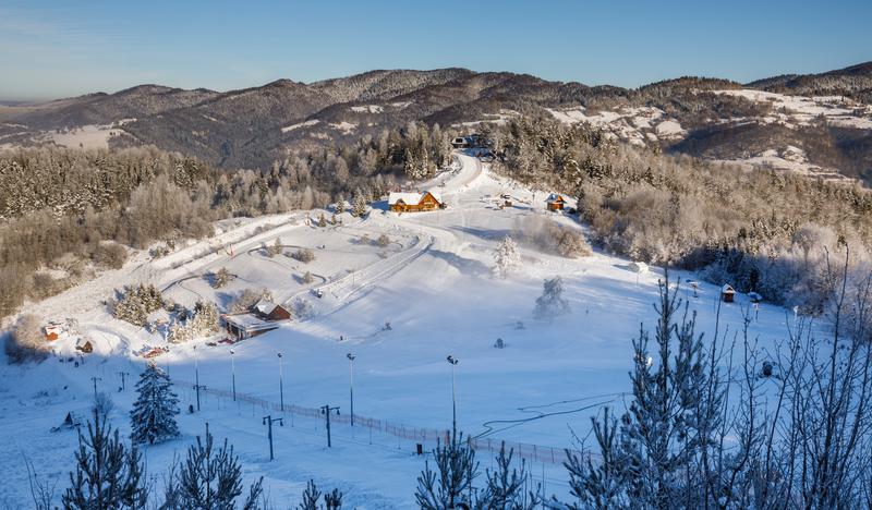 Wyciąg narciarski oraz kilka budynków na polanie zasypanej śniegiem.