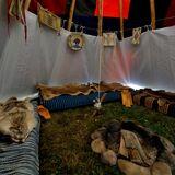 Wnętrze indiańskiego namiotu, gdzie na środku znajduje się palenisko, a wokół niego niskie łóżka nakryte skórami
