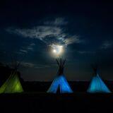 Indiańskie namioty podświetlone na kolor zielony i niebieski nocą przy świetle księżyca