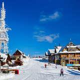 Widok na stację narciarską Jaworzyna Krynicka w słoneczny zimowy dzień, w tle zaplecze gastronomiczne i inne obiekty