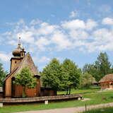 Drewniany kościół i chata w otoczeniu zieleni na terenie Nadwiślańskiego Parku Etnograficznego w Wygiełzowie