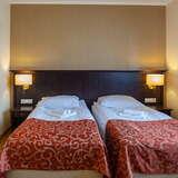Pokój z dwoma pojedynczymi łóżkami, zasłanym bordowymi, ozdobnymi kapami, na ścianie obraz.
