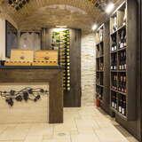 Wnętrze restauracji Bottiglieria 1881 w Krakowie.  lewej ustawiona półka z winami. Na wprost bar, na którym w drewnianych skrzyniach ustawione są wina.
