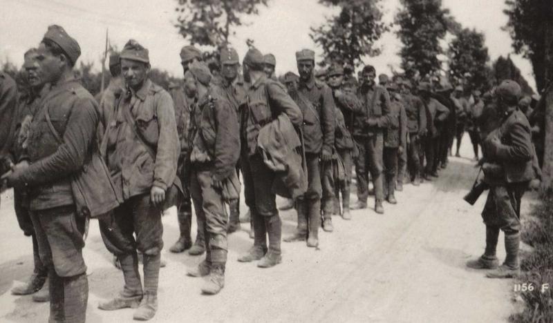 Zdjęcie archiwalne, czarno-białe. Kolumna żołnierzy idących drogą.
